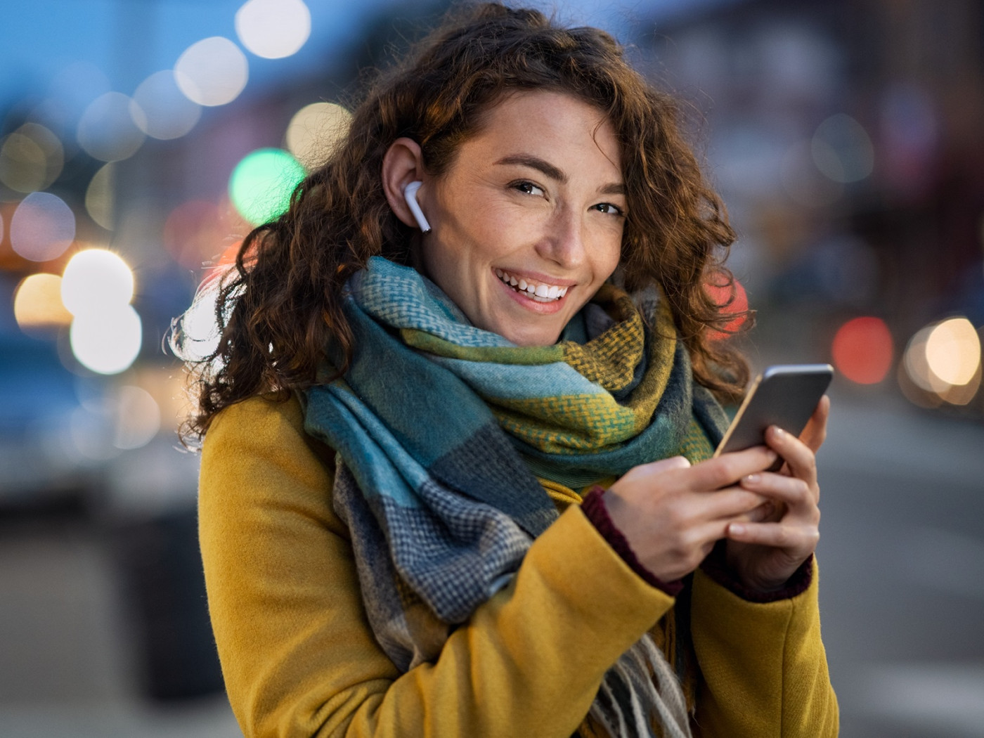 Woman in warm clothes on city street texting with earpiece in