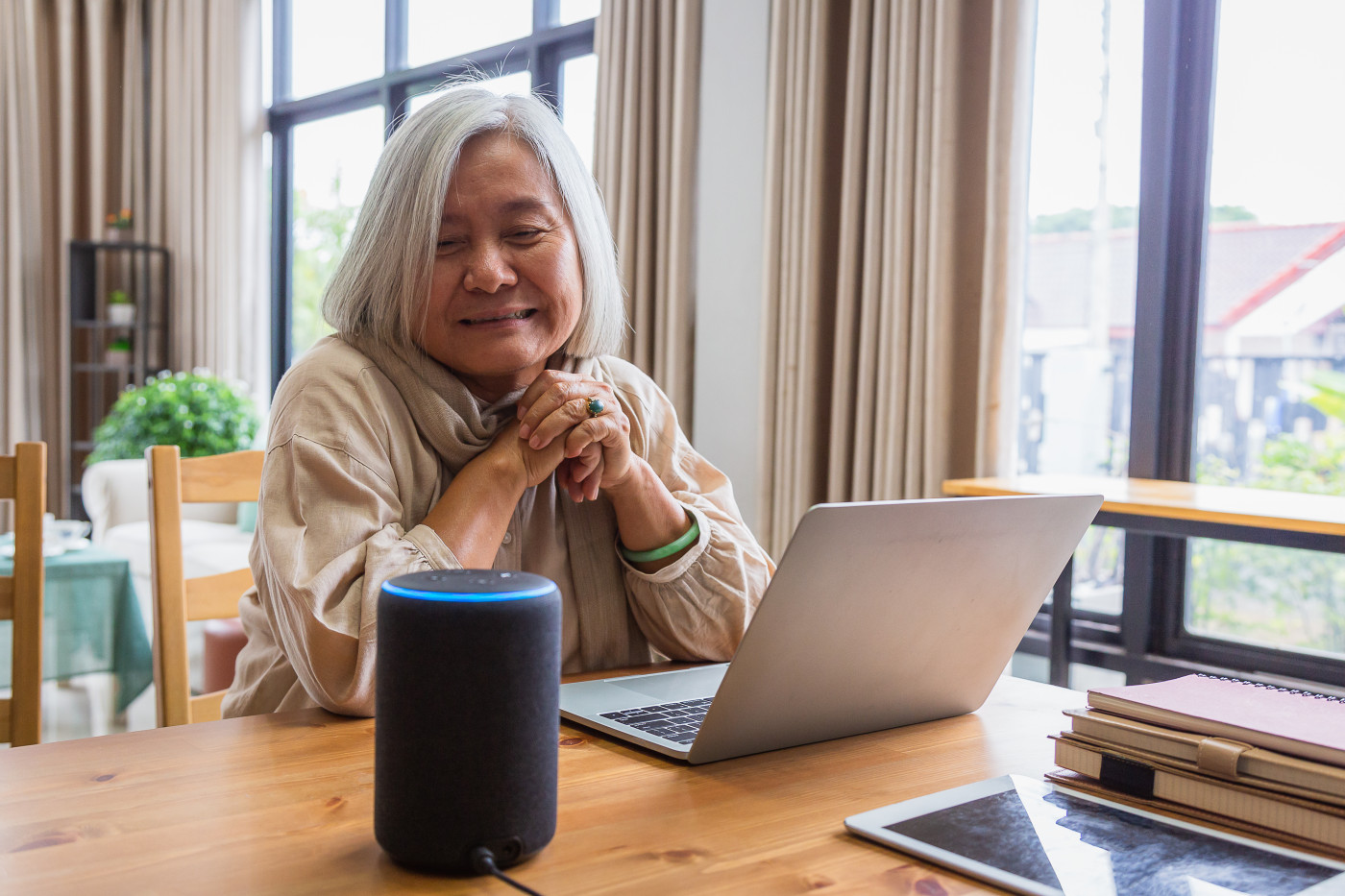 Senior woman working with laptop computer and using smart speakers while setting in living room at home